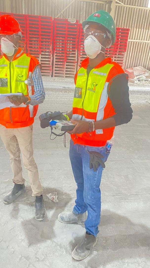 Consultants in hard hats and respirators operating a monitoring instrument in a warehouse